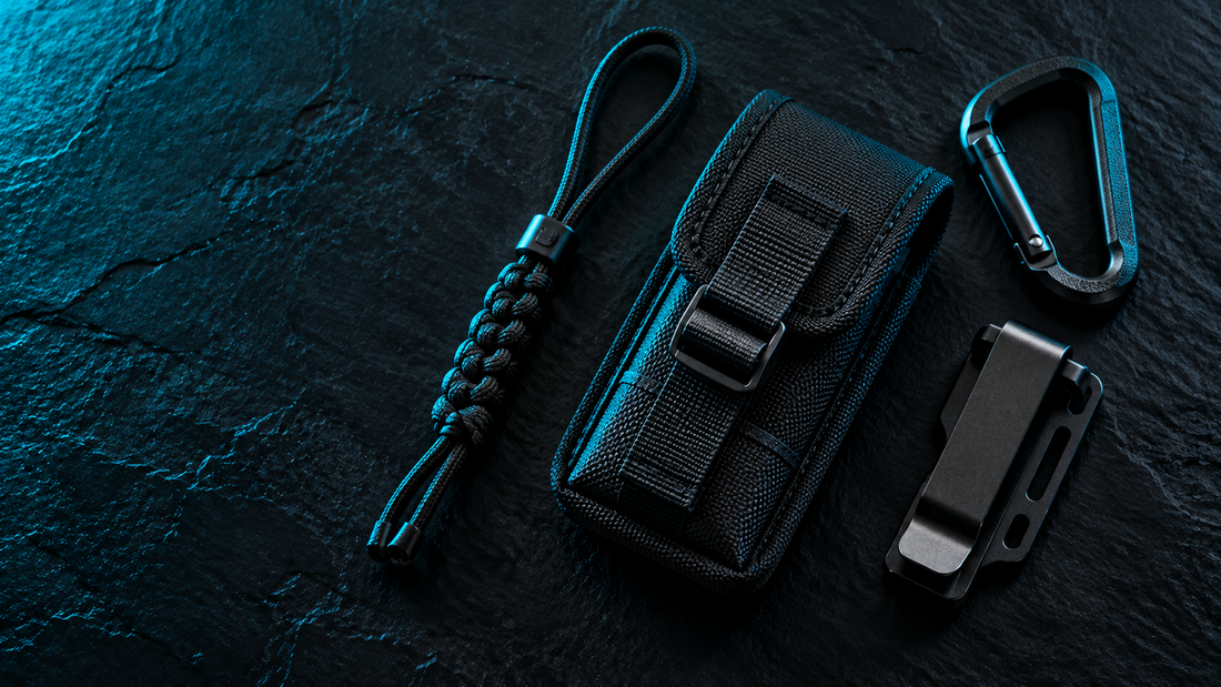 Flat lay of a black pouch, paracord lanyard, carabiner and belt clip on black slate with cyan edge light