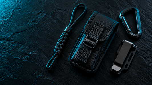 Flat lay of a black pouch, paracord lanyard, carabiner and belt clip on black slate with cyan edge light