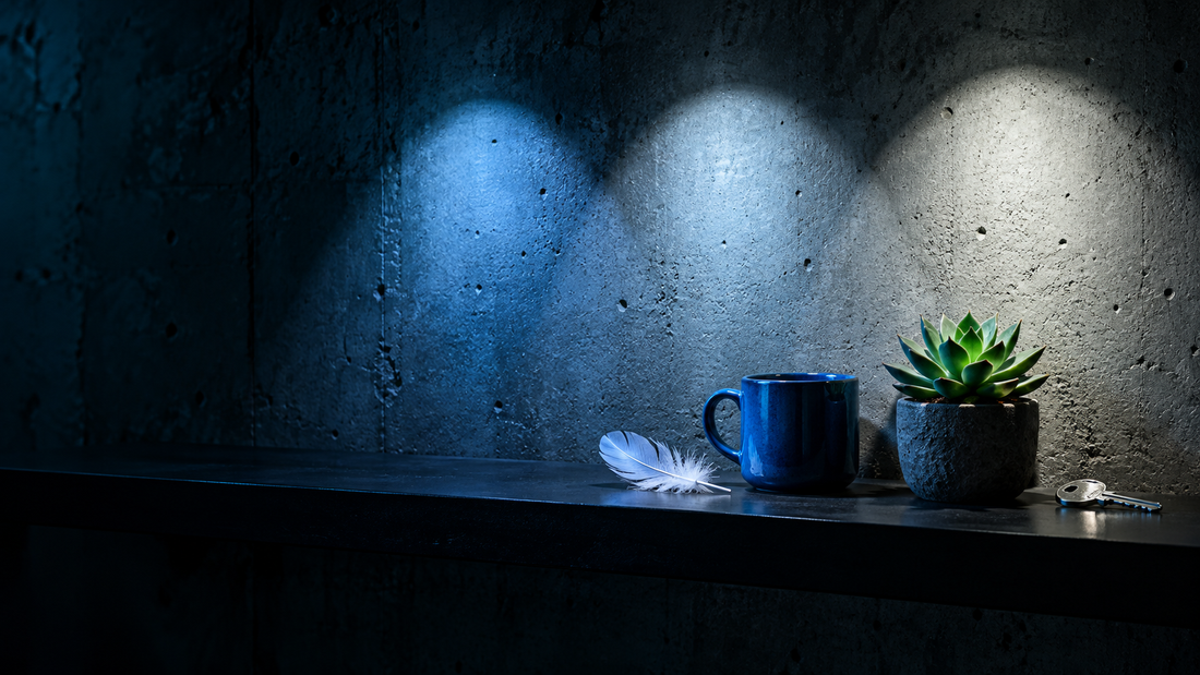 Three pools of blue-white light on a concrete wall lighting colorful objects on a shelf