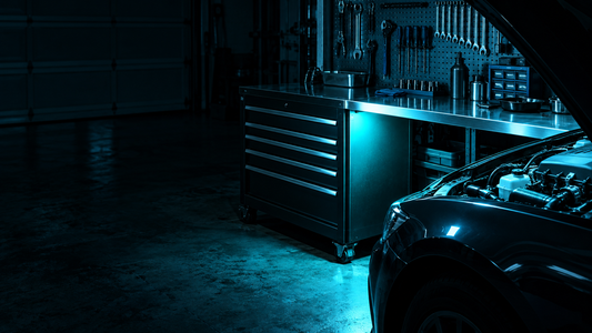 Dark home garage with a black steel toolbox and workbench lit by a wide even flood of cyan-white light